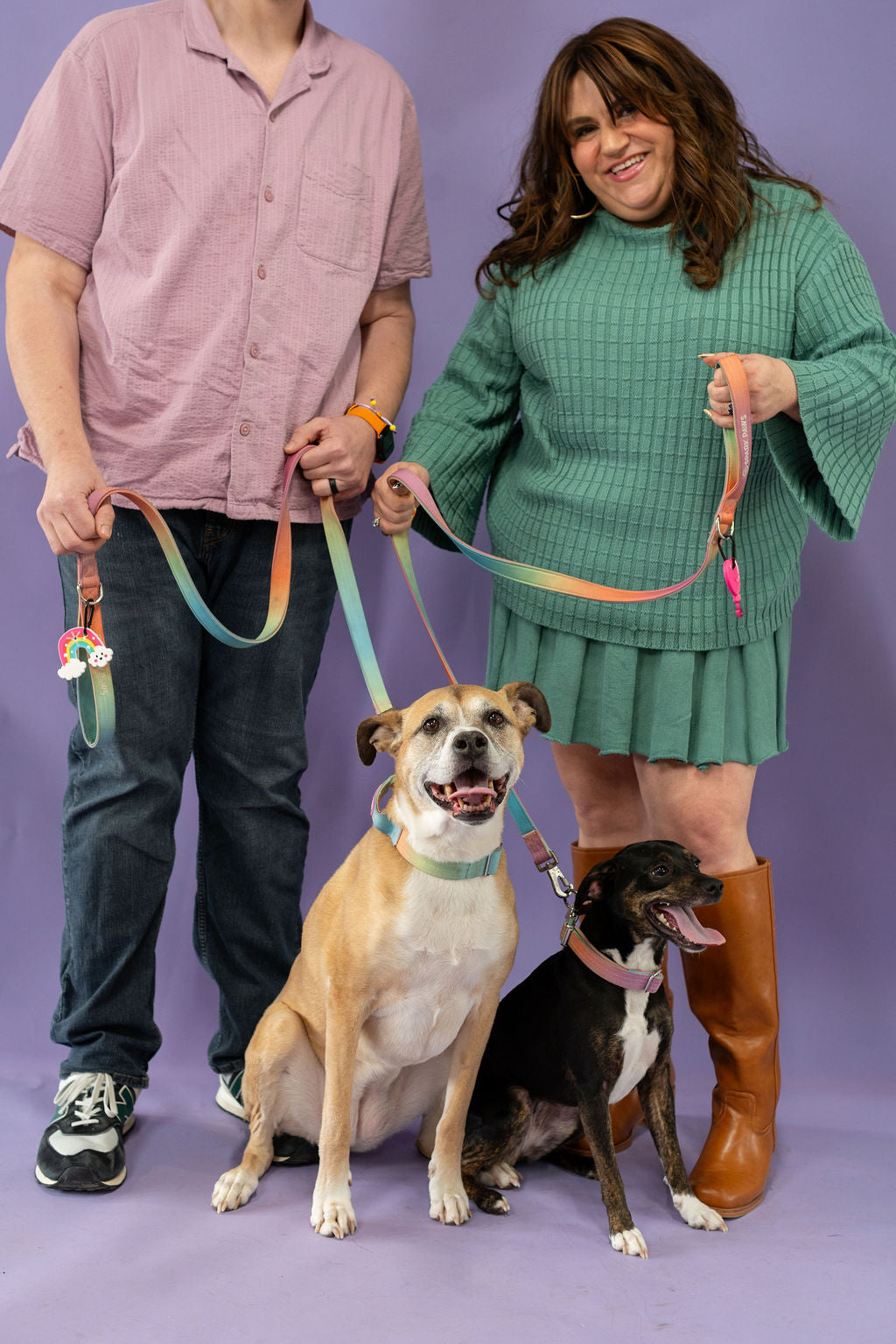 Two people with two dogs on leashes against a purple background