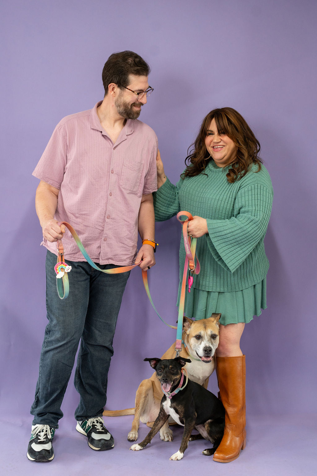 Man and woman standing with two dogs on leashes against a purple background
