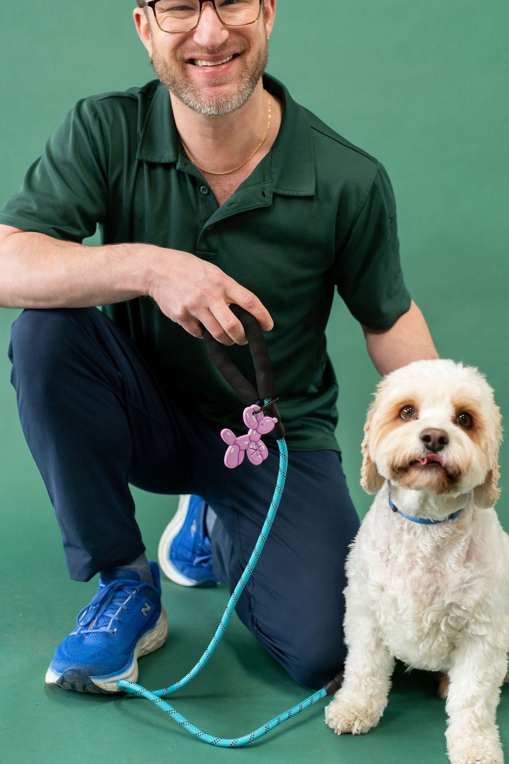 Man in green shirt and blue pants kneeling with a dog on a green background