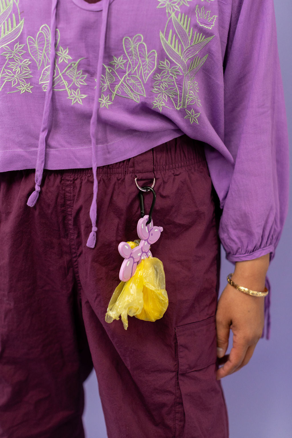 Person wearing a purple outfit with floral embroidery, holding a yellow bag with a pink flower charm.