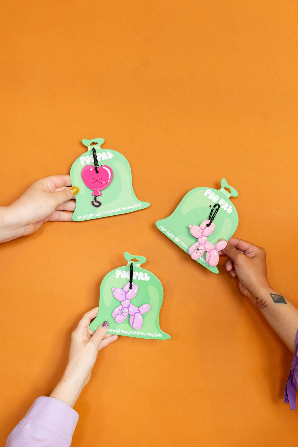 Three green pouches with pink hearts and flowers on an orange background