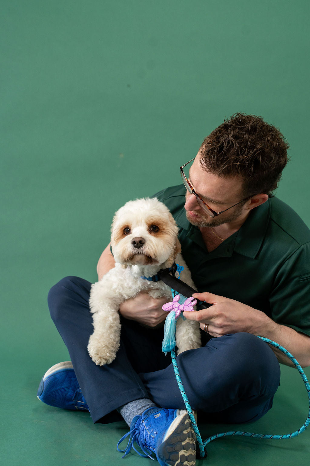 Man sitting on the floor with a small white dog against a green background