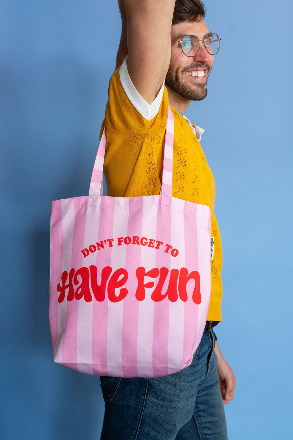 Man holding a pink and white striped tote bag with 'Don't Forget to Have Fun' text against a blue background