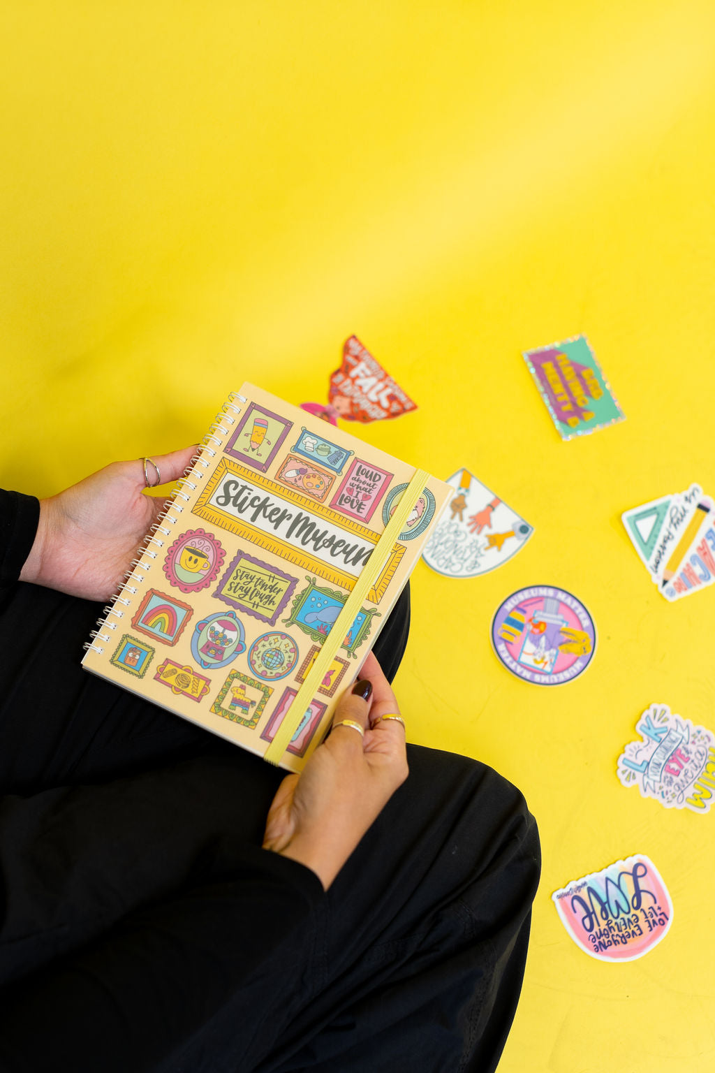 Person holding a sticker book with colorful stickers on a yellow background