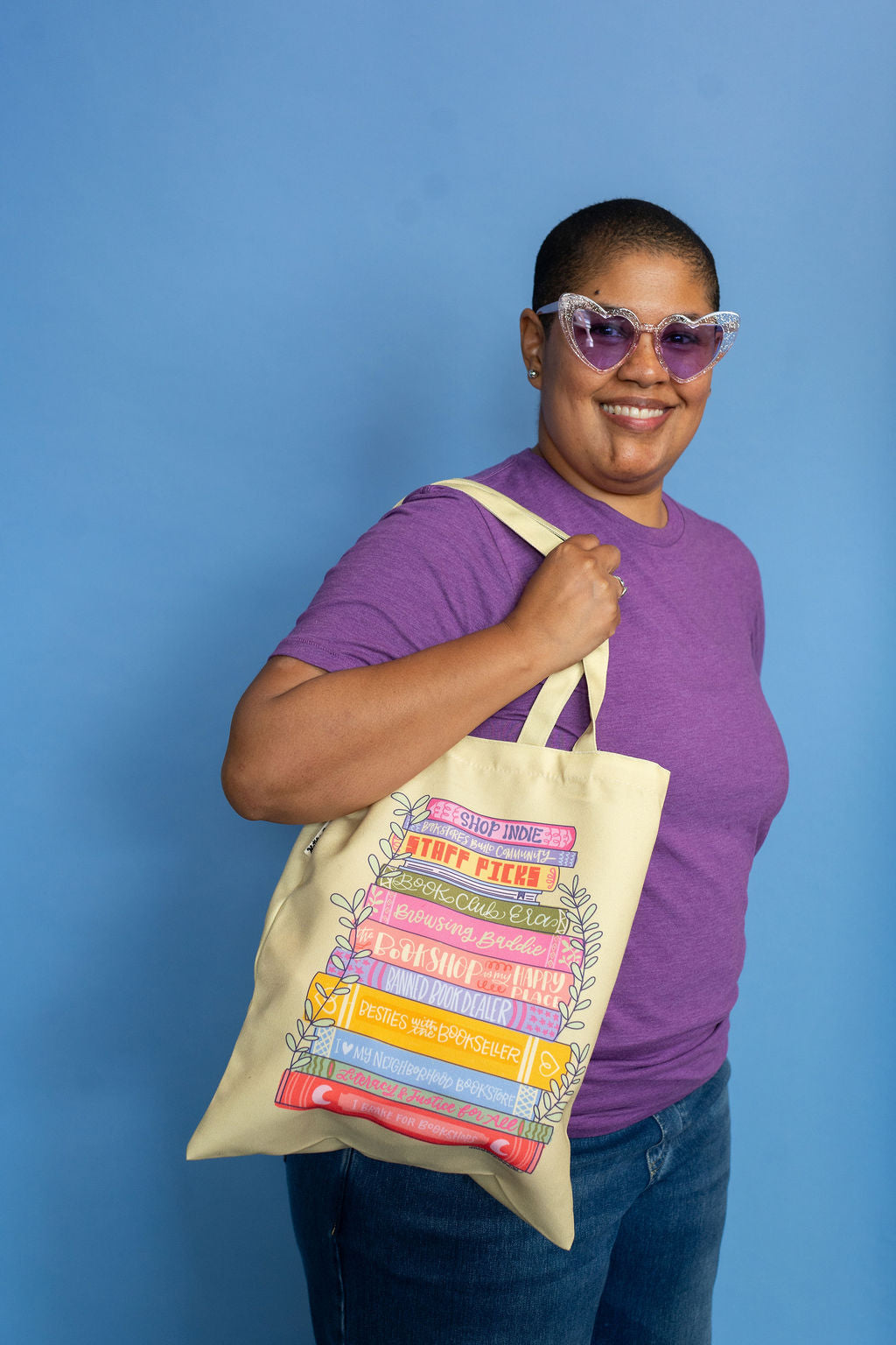 Person holding a tote bag with colorful book design against a blue background
