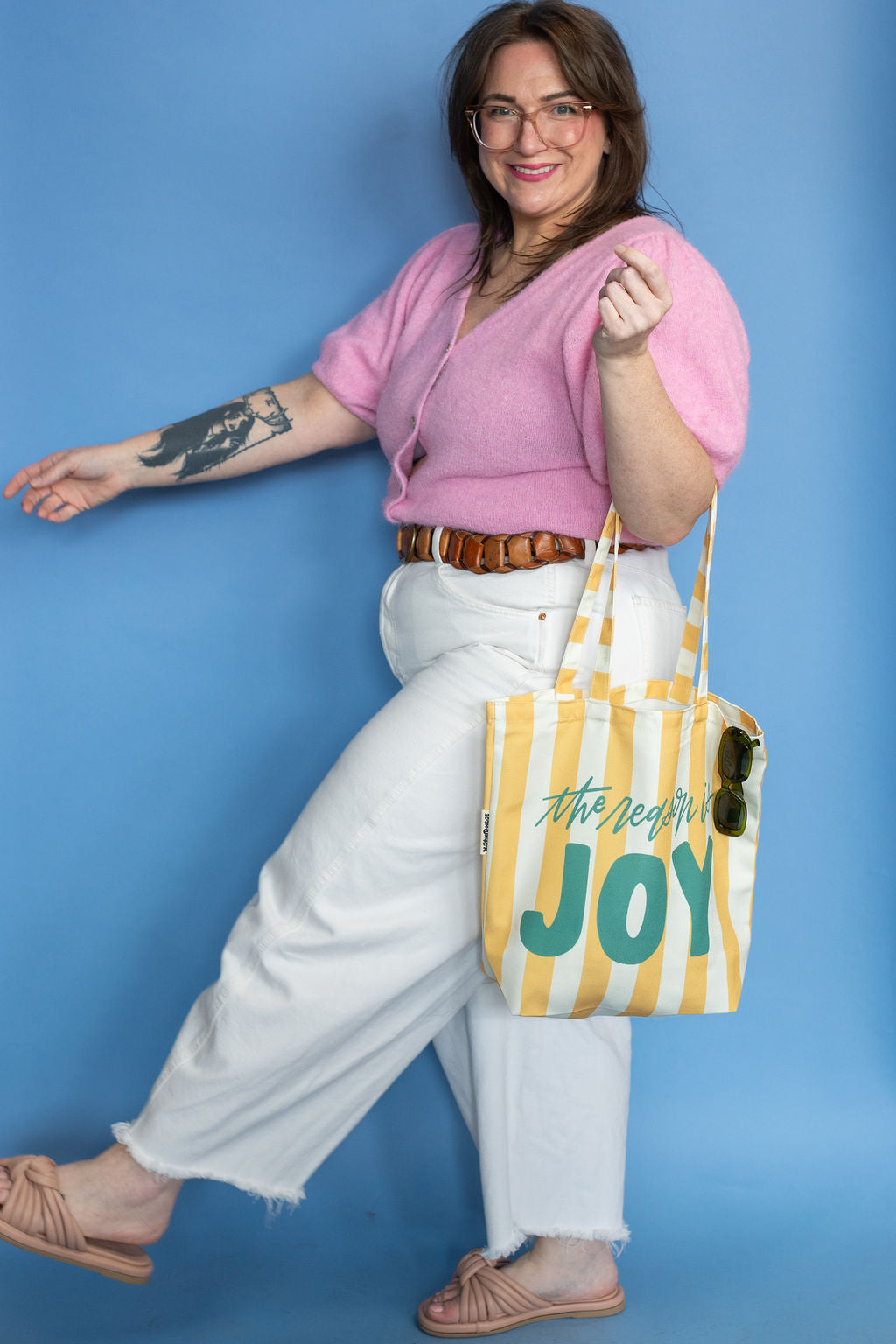 Woman holding a striped tote bag with 'the reason is joy' text against a blue background