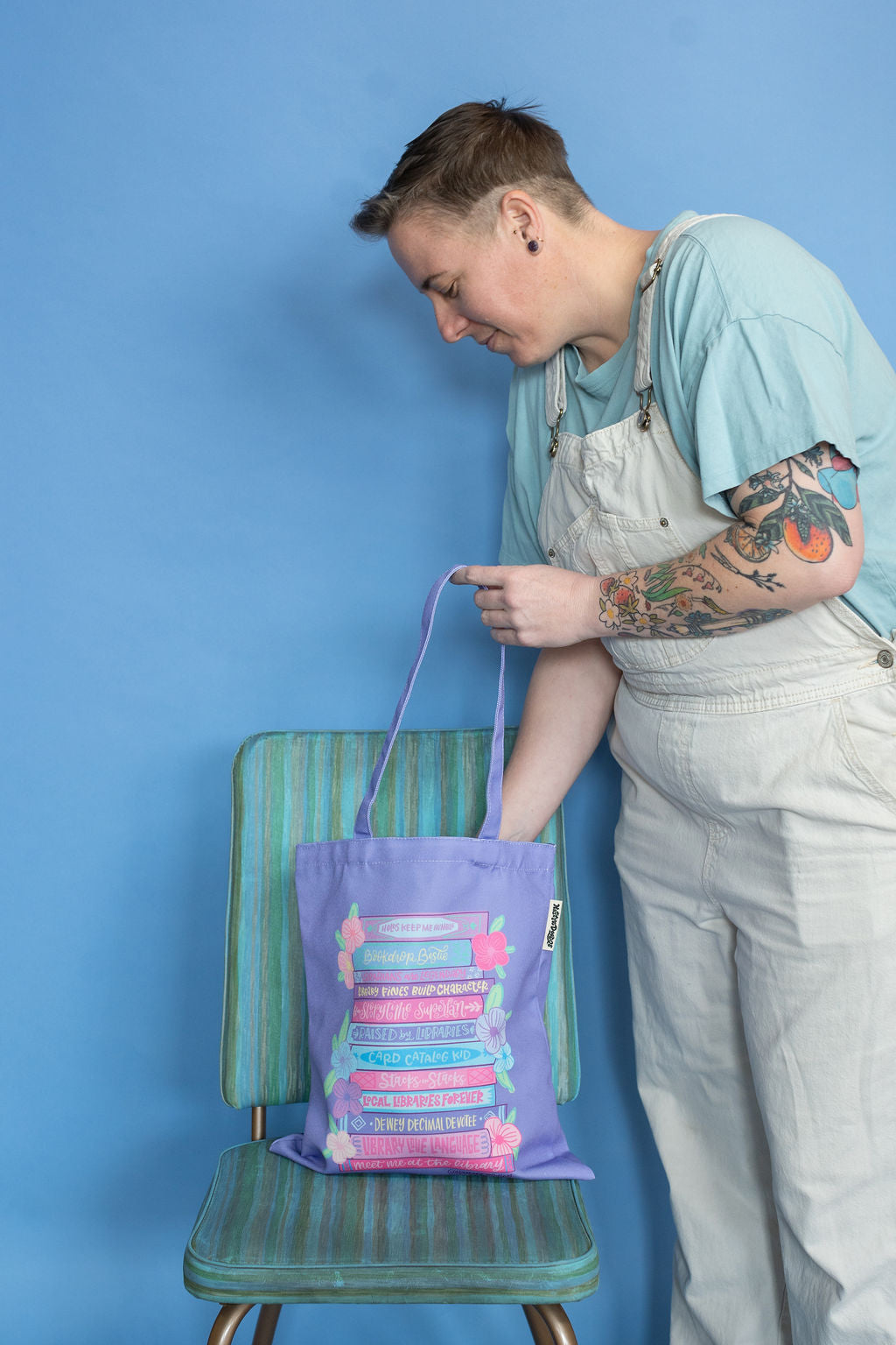 Person holding a purple tote bag with book design against a blue background