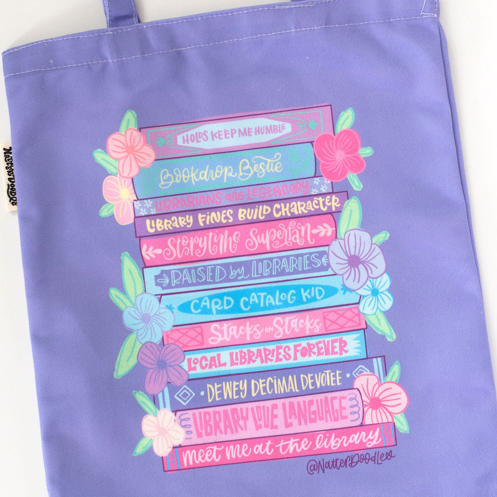 Purple tote bag with colorful text and floral designs on a white background