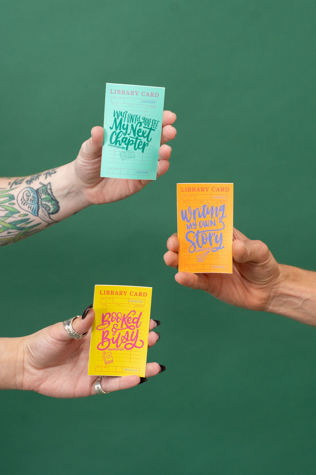 Three colorful stckers held by hands against a green background