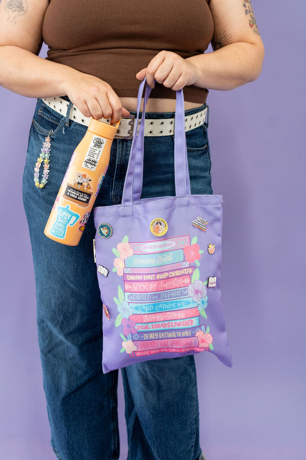 Person holding a purple tote bag with colorful designs against a purple background