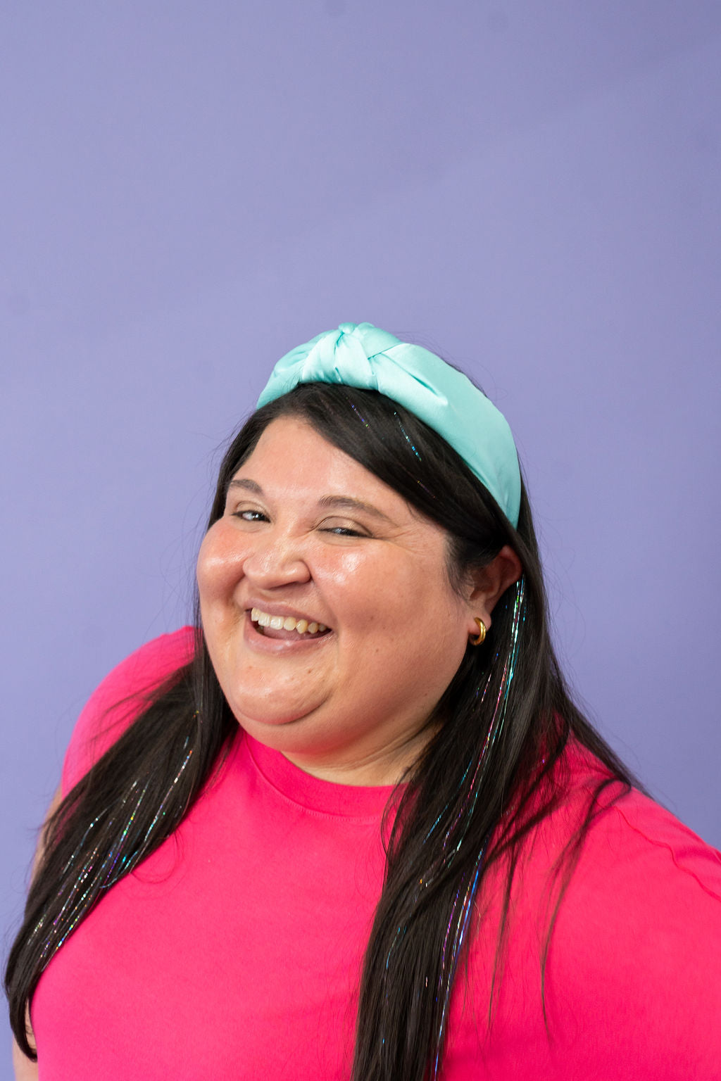 Person wearing a bright pink shirt and turquoise headband against a purple background