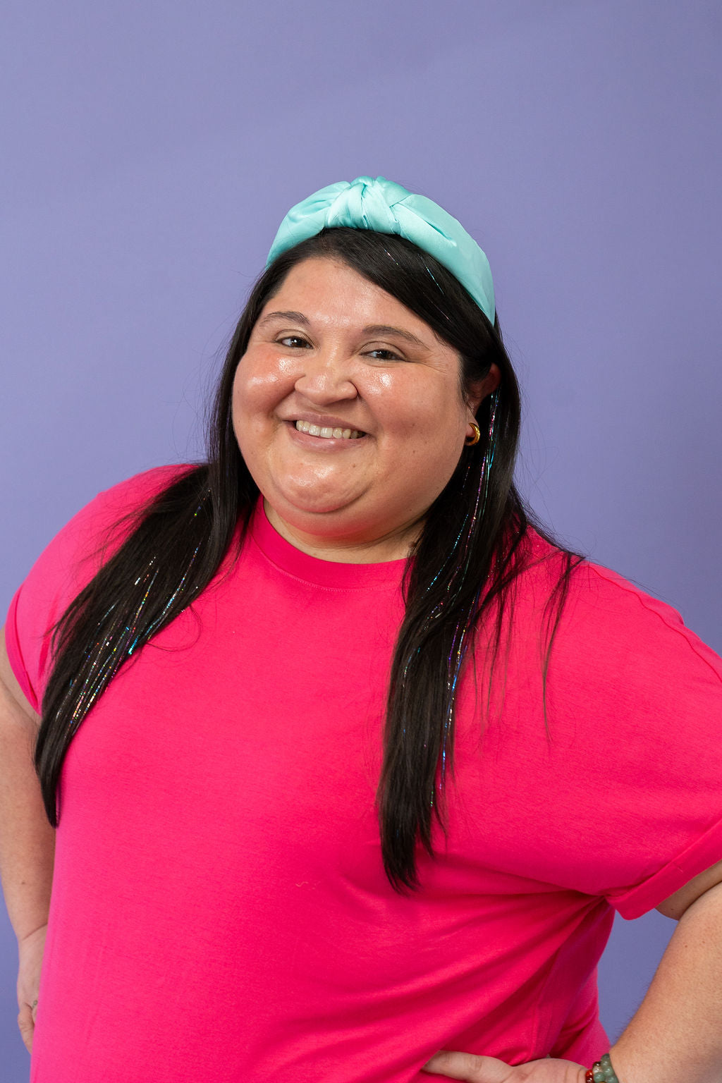 Person wearing a bright pink shirt and teal headband against a purple background