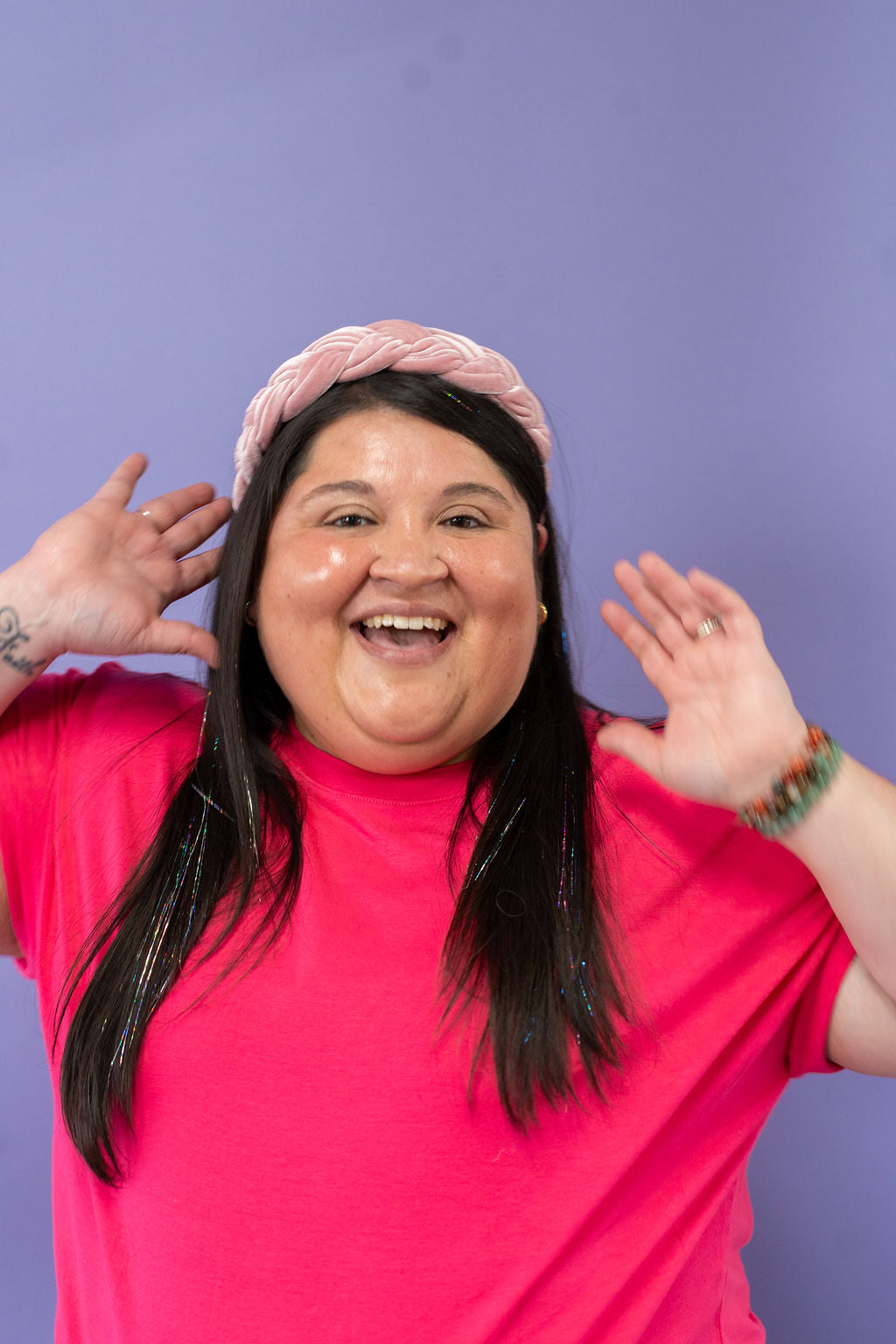 Person wearing a pink shirt and headband against a purple background