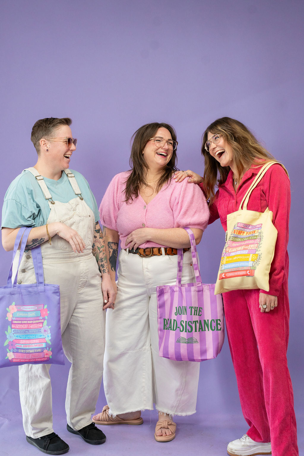 Three people standing together holding colorful bags against a purple background