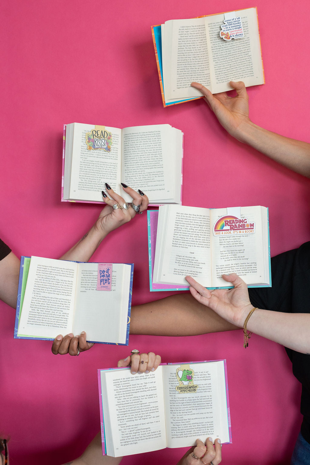 Four people holding open books against a pink background