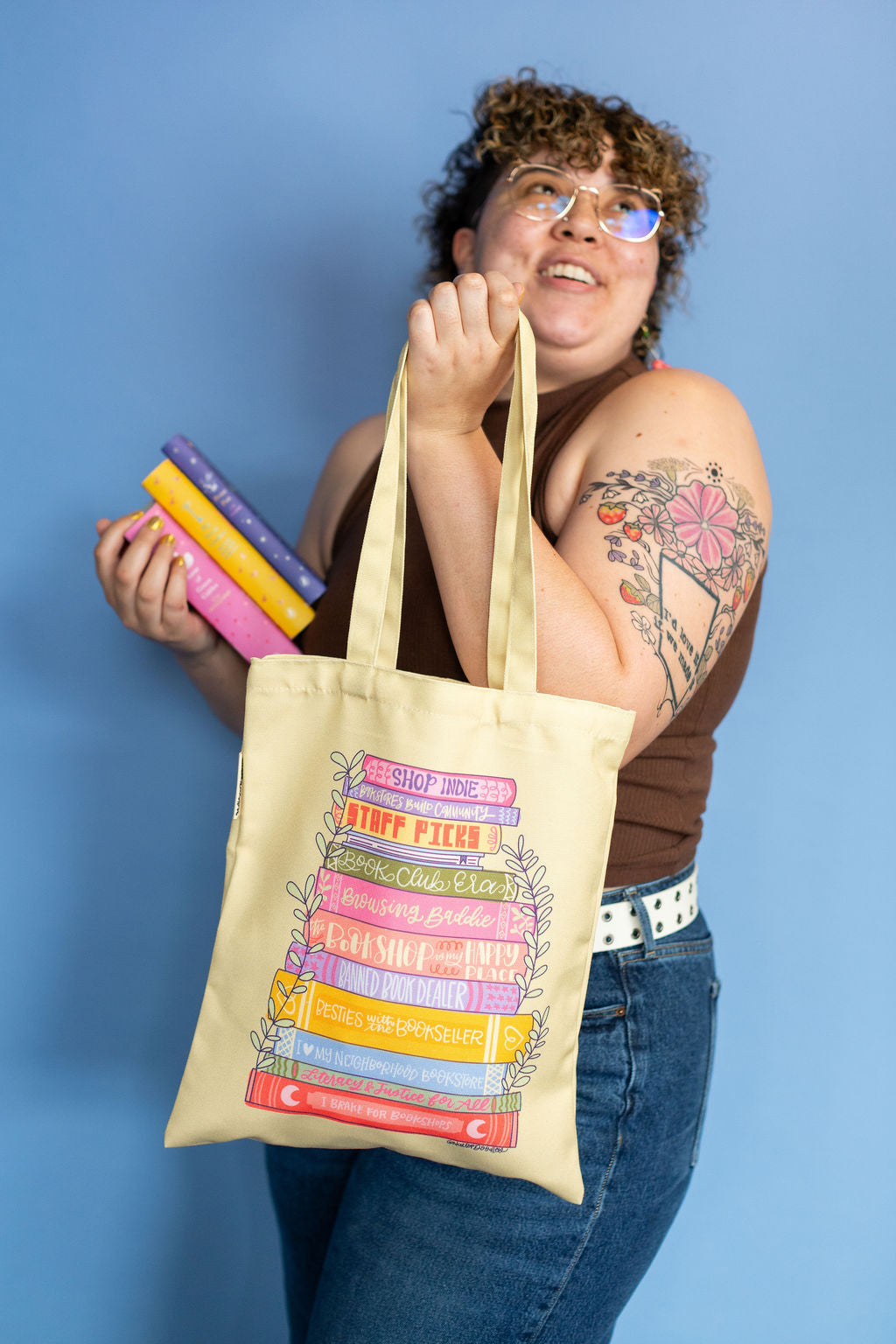 Person holding a tote bag with colorful book design against a blue background