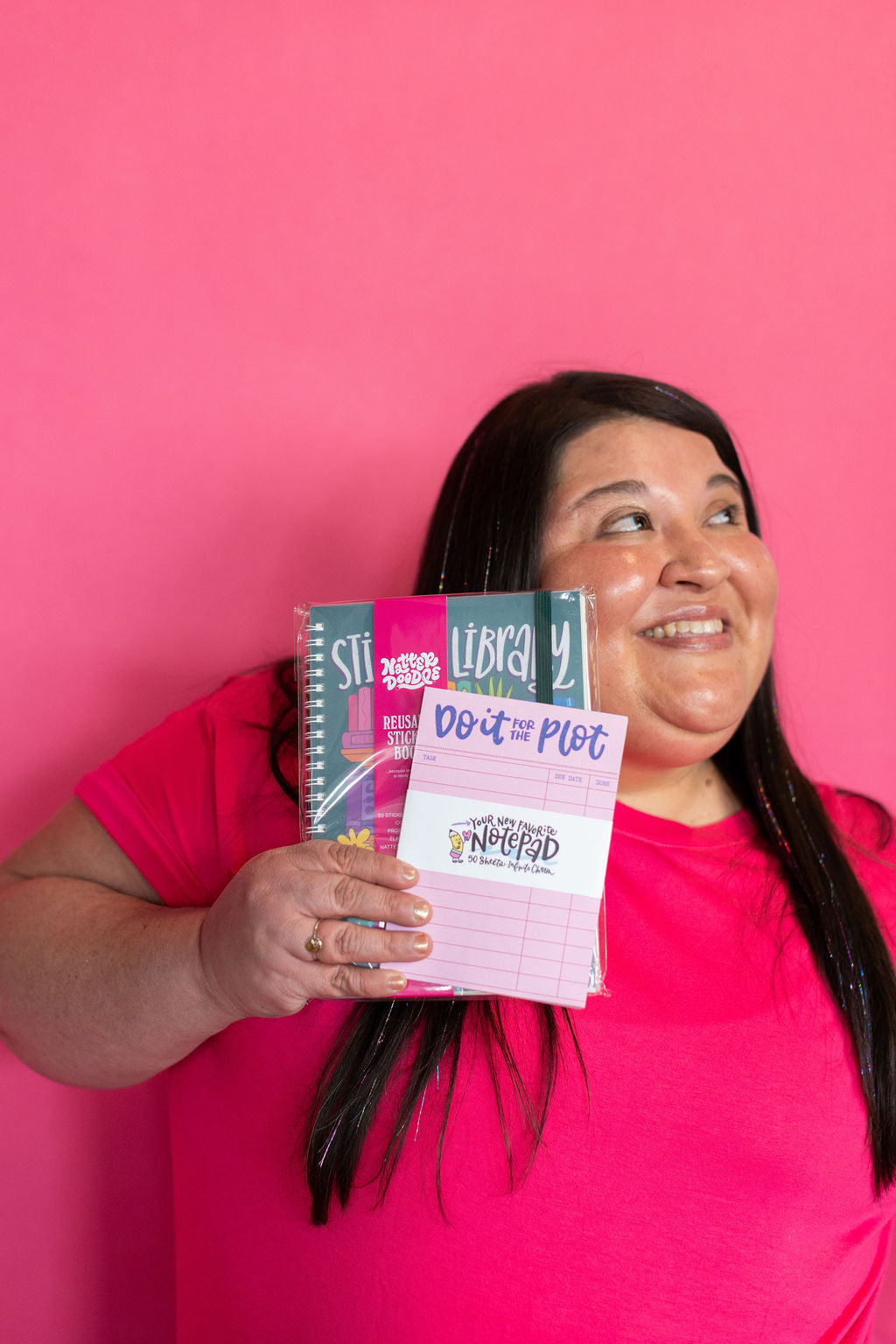 Person holding a book titled 'Do the Plot' against a pink background