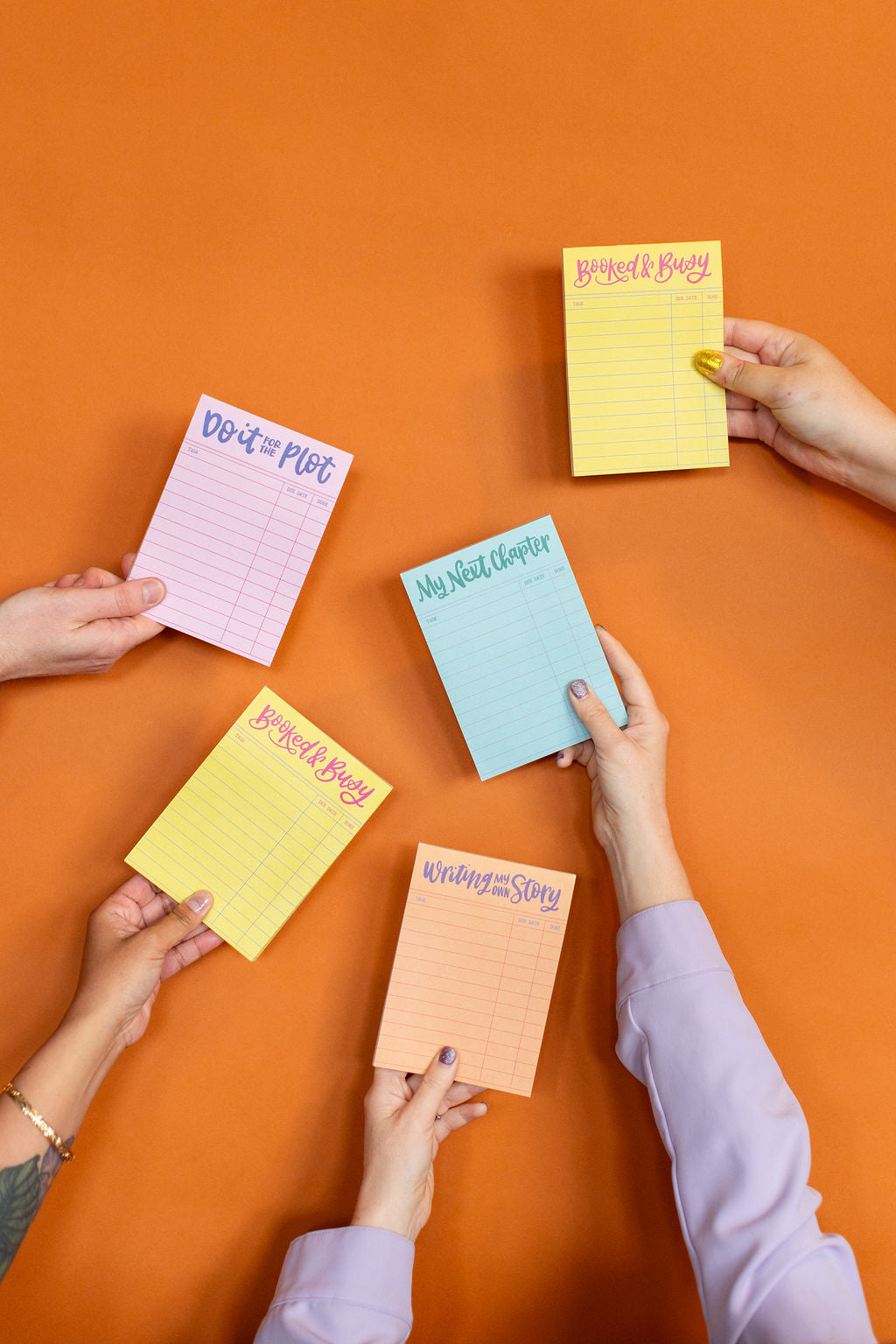 Hands holding colorful notepads on an orange background