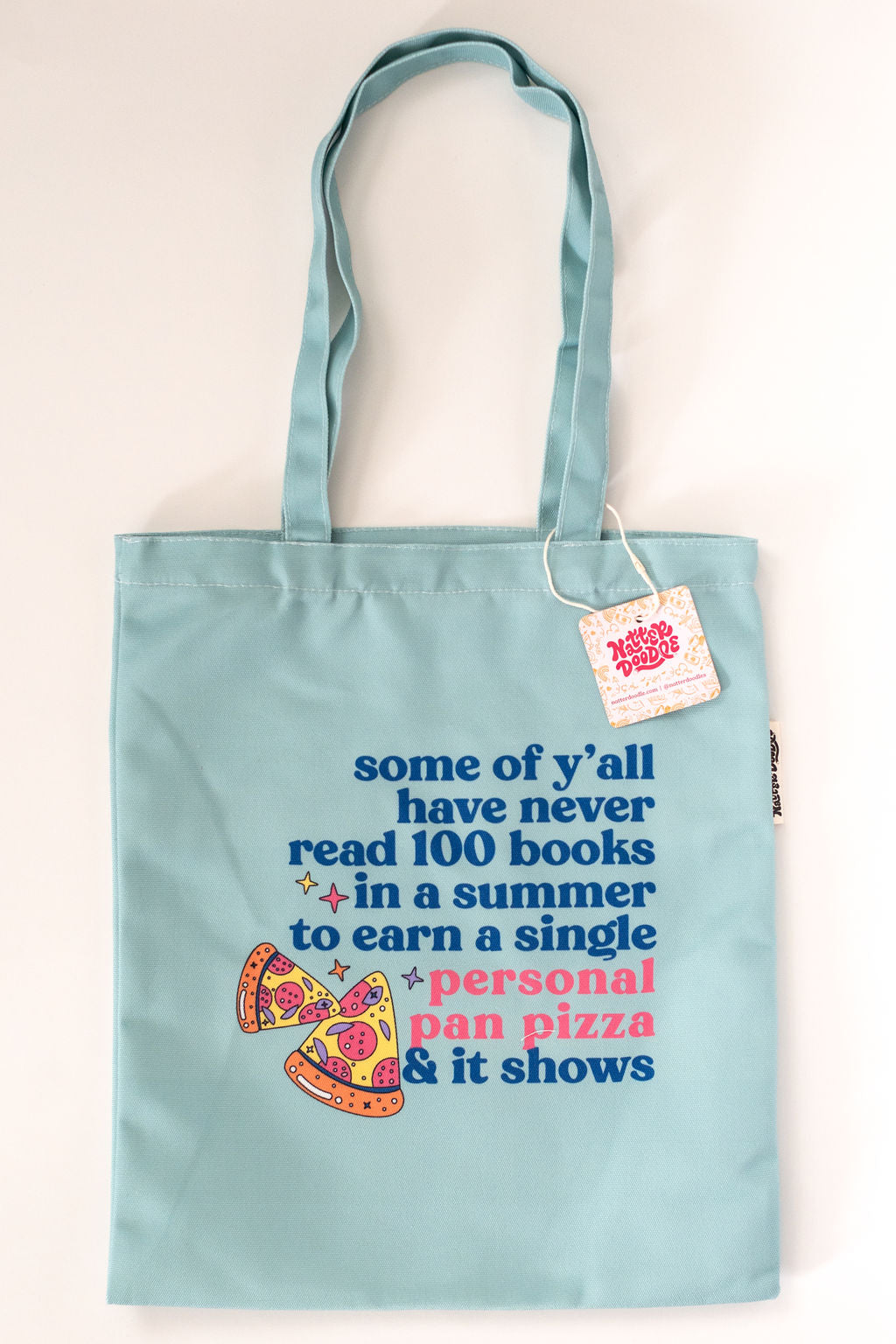 Light blue tote bag with text and pizza graphic on a white background