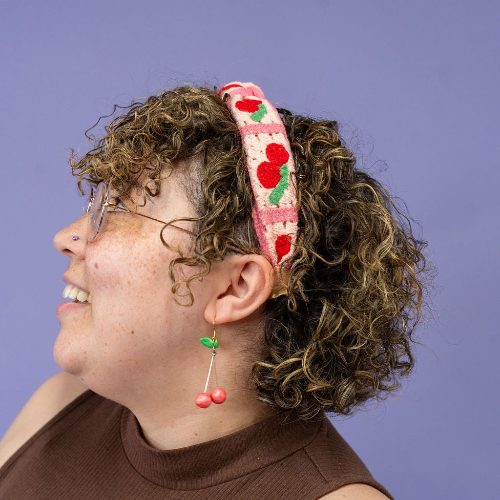 Person wearing a headband with cherry design against a purple background
