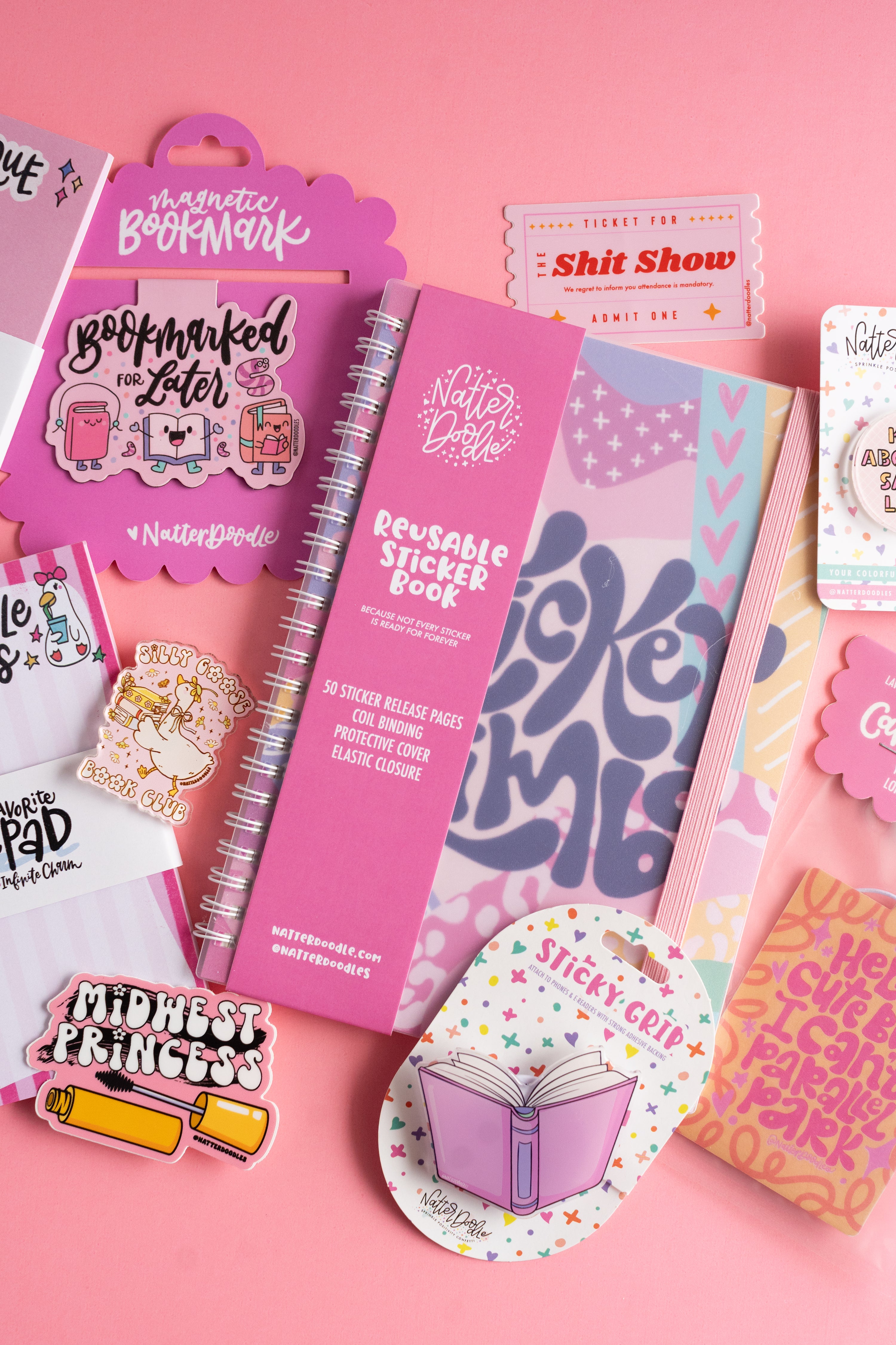 Collection of stationery items including a pink notebook, stickers, and magnetic bookmarks on a pink background.