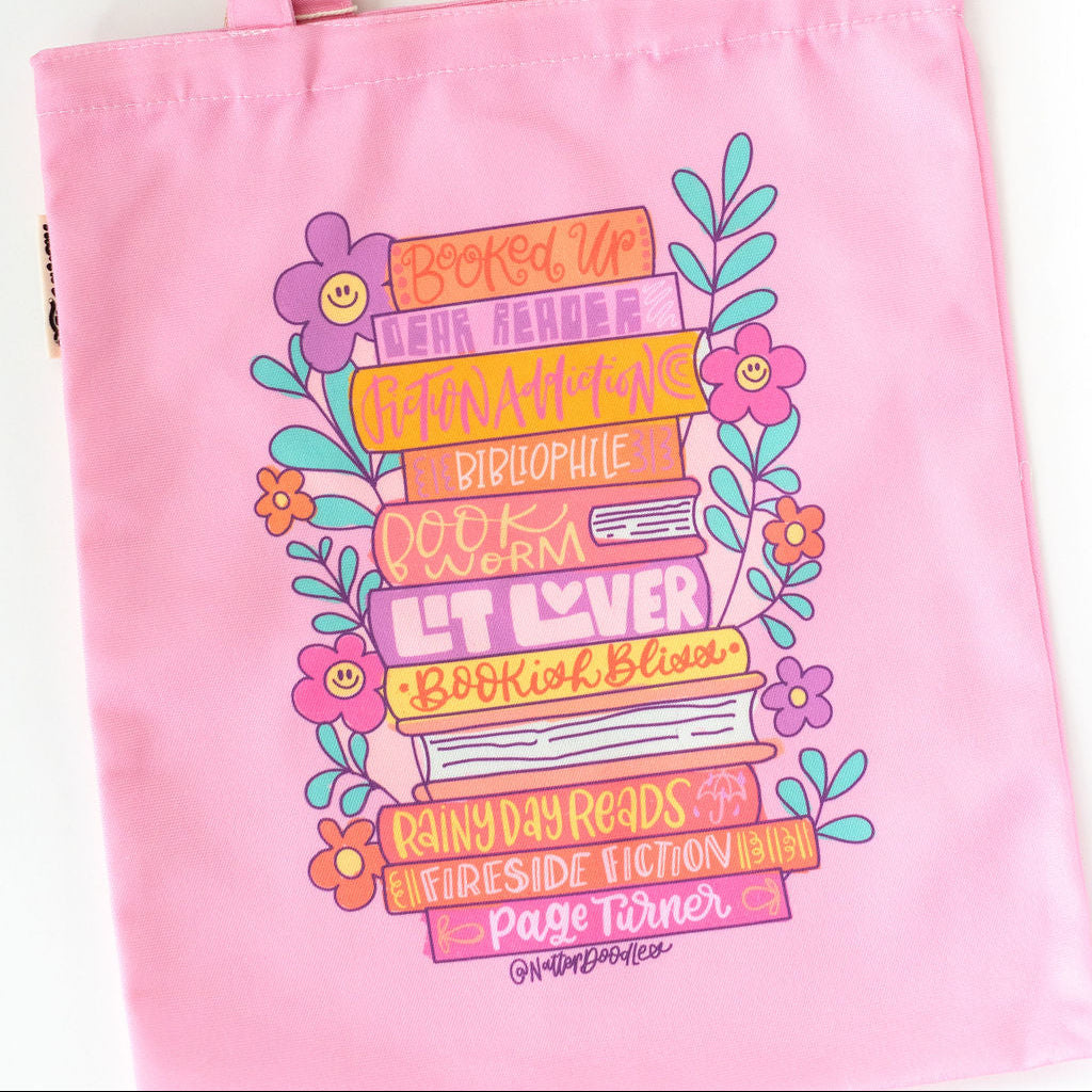 Pink tote bag with colorful book-themed design on a white background