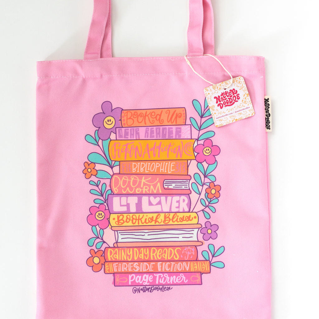 Pink tote bag with colorful book design and text on a white background