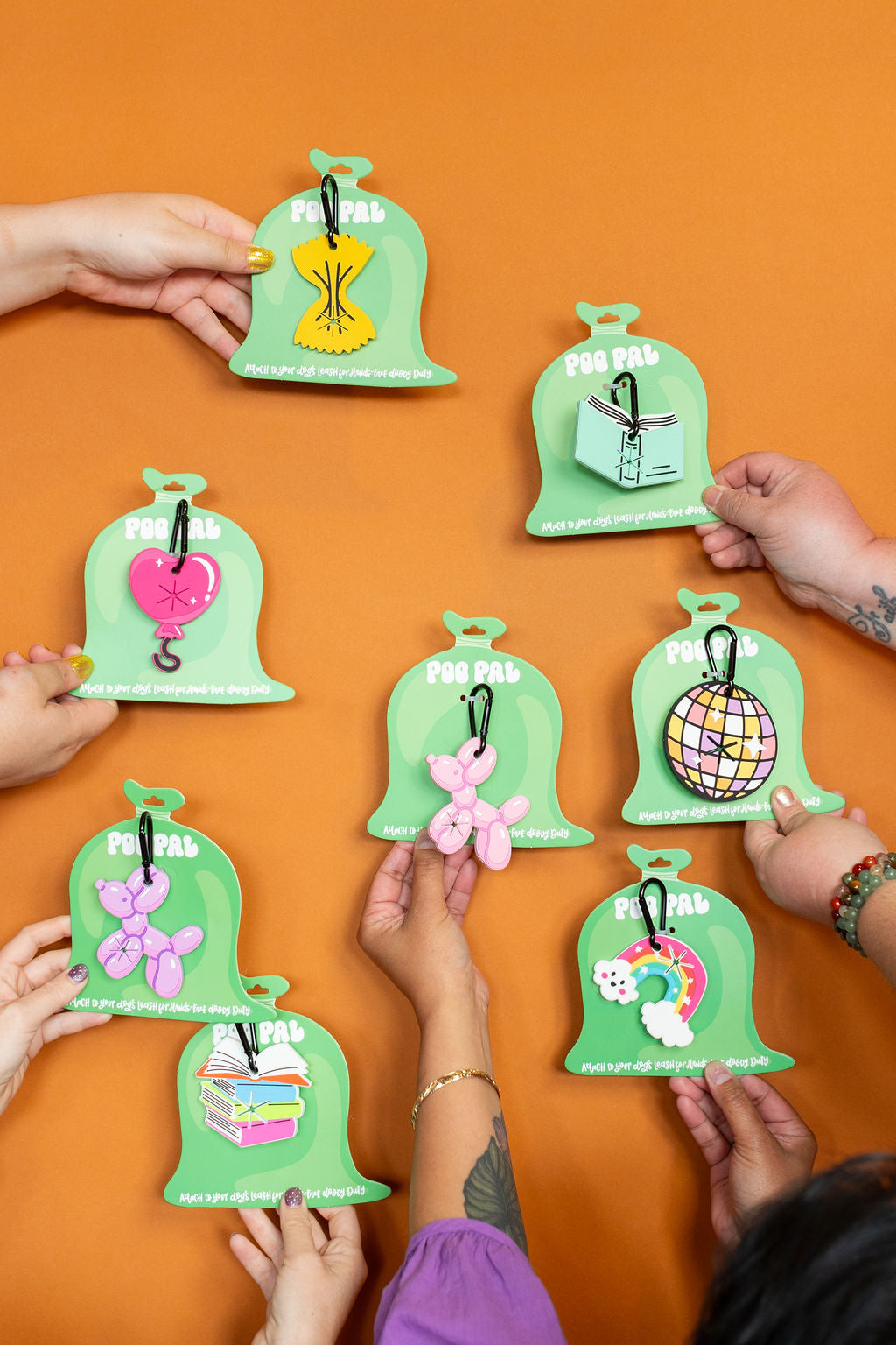 Green poo pal packaging with colorful dog accessories on an orange background