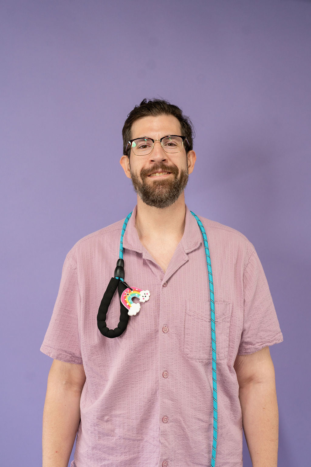 Person wearing a pink shirt with a leash and a colorful poo palon a purple background