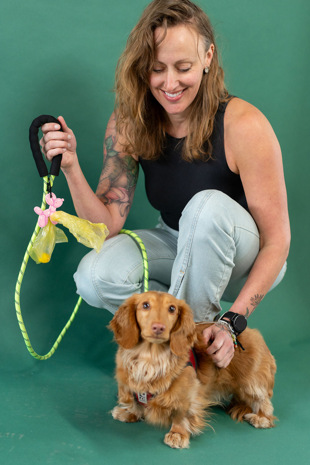 Woman with tattoos sitting on a green background with small dog and a green leash.