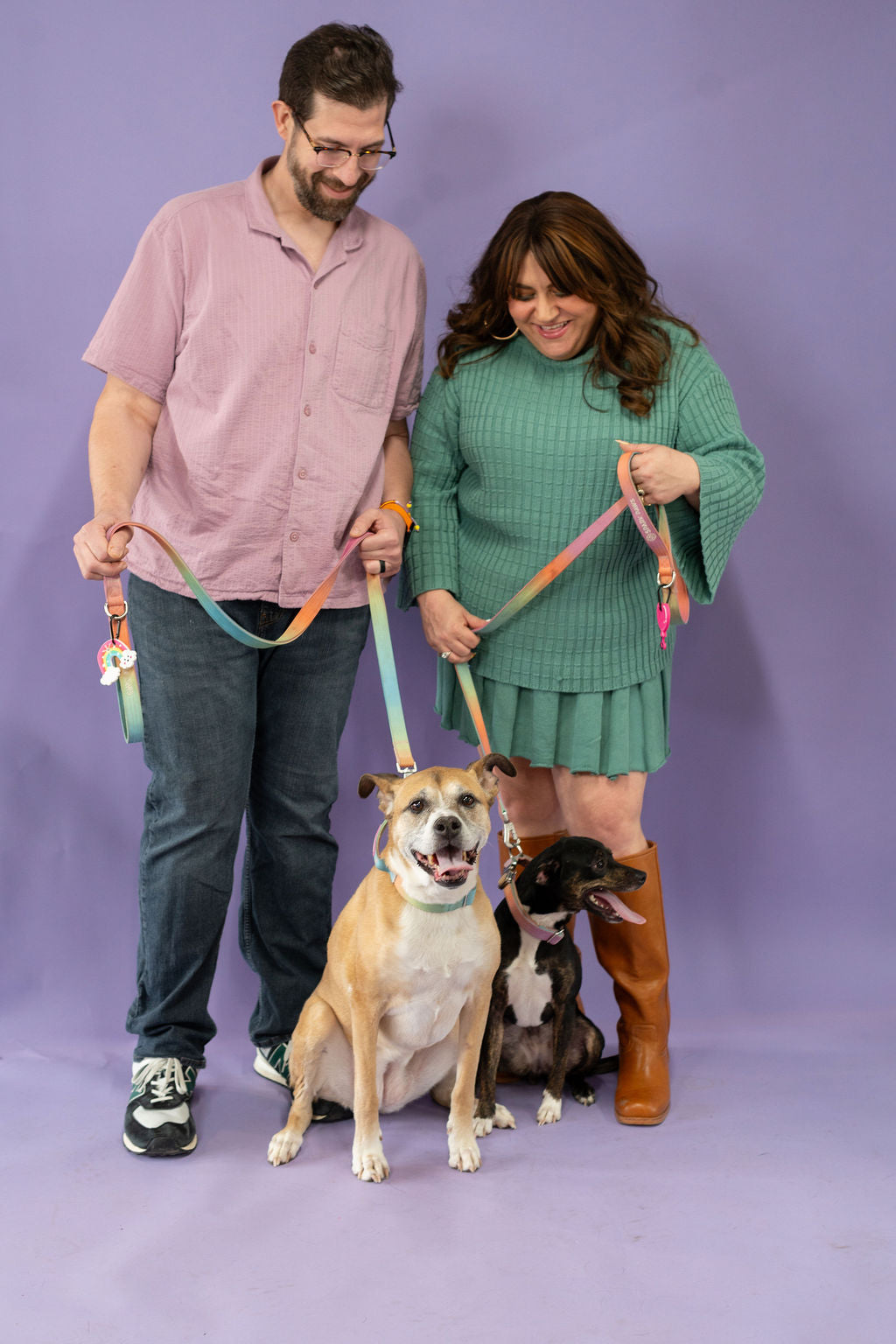 Man and woman holding leashes with two dogs against a purple background