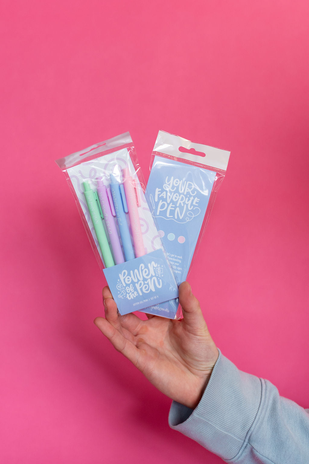 Hand holding a set of colorful pens in packaging against a pink background