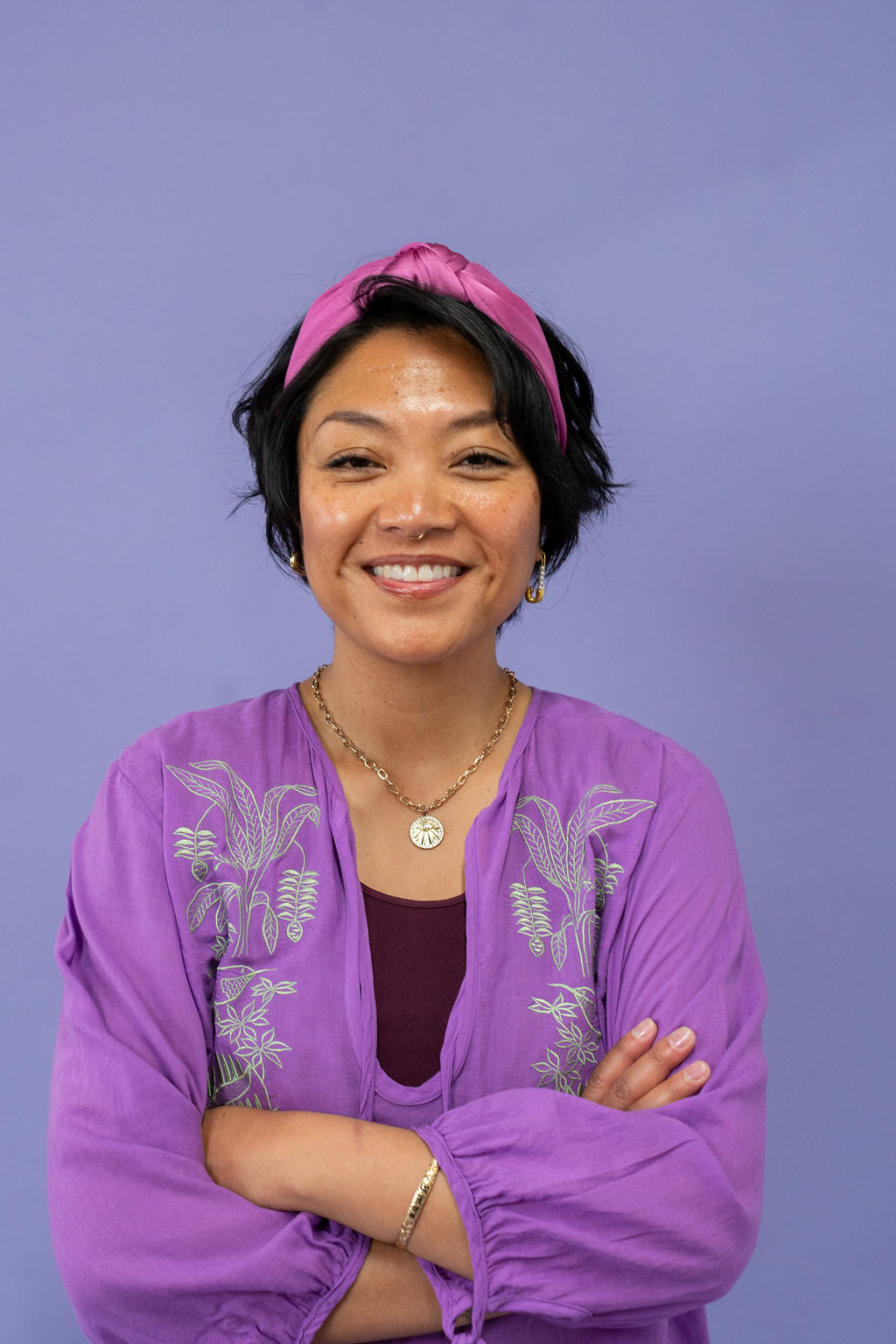 Woman wearing a purple embroidered jacket and pink headscarf against a purple background