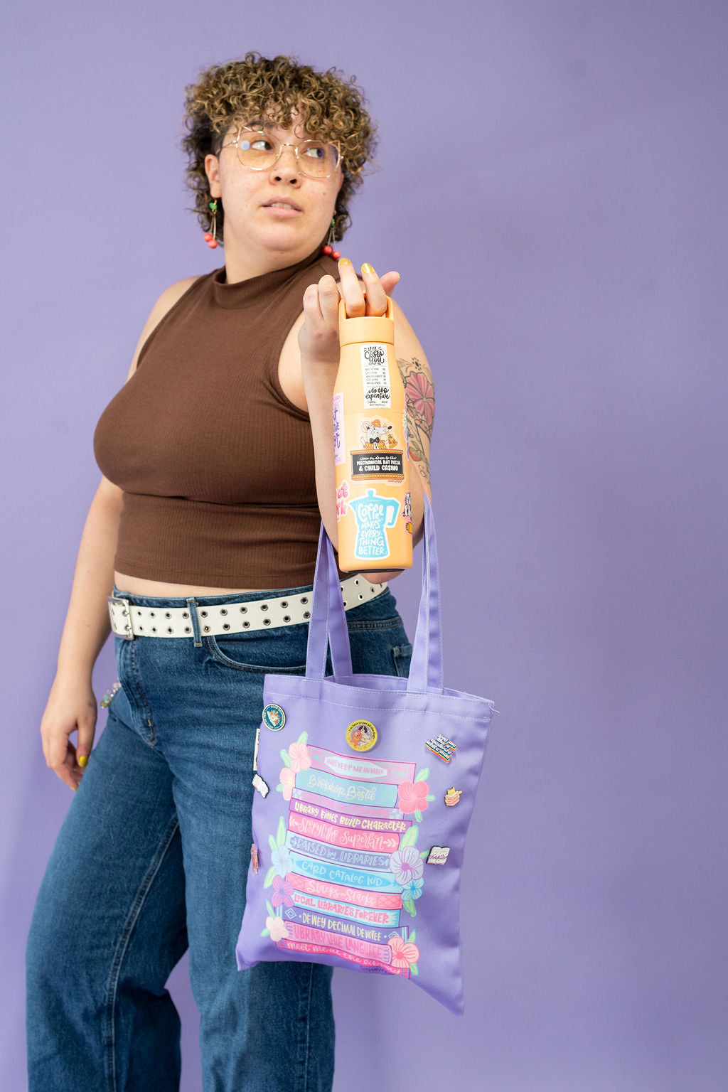 Person holding a bottle of shampoo and a purple tote bag against a purple background