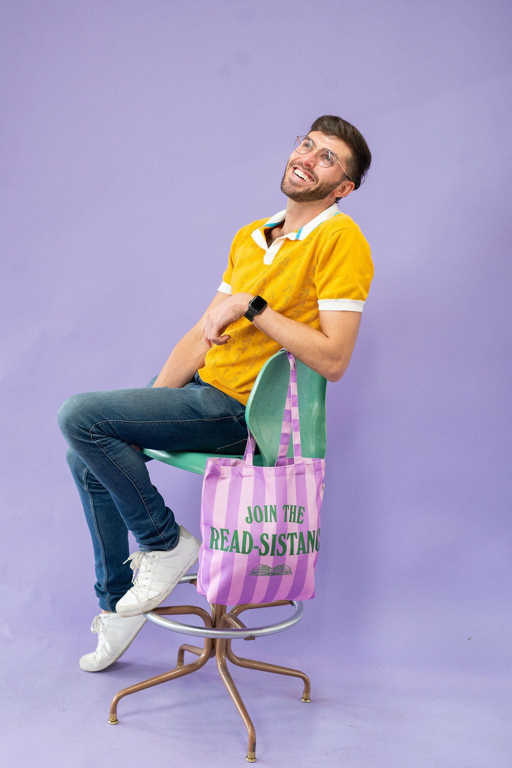 Man sitting on a chair with a purple tote bag featuring text on a purple background