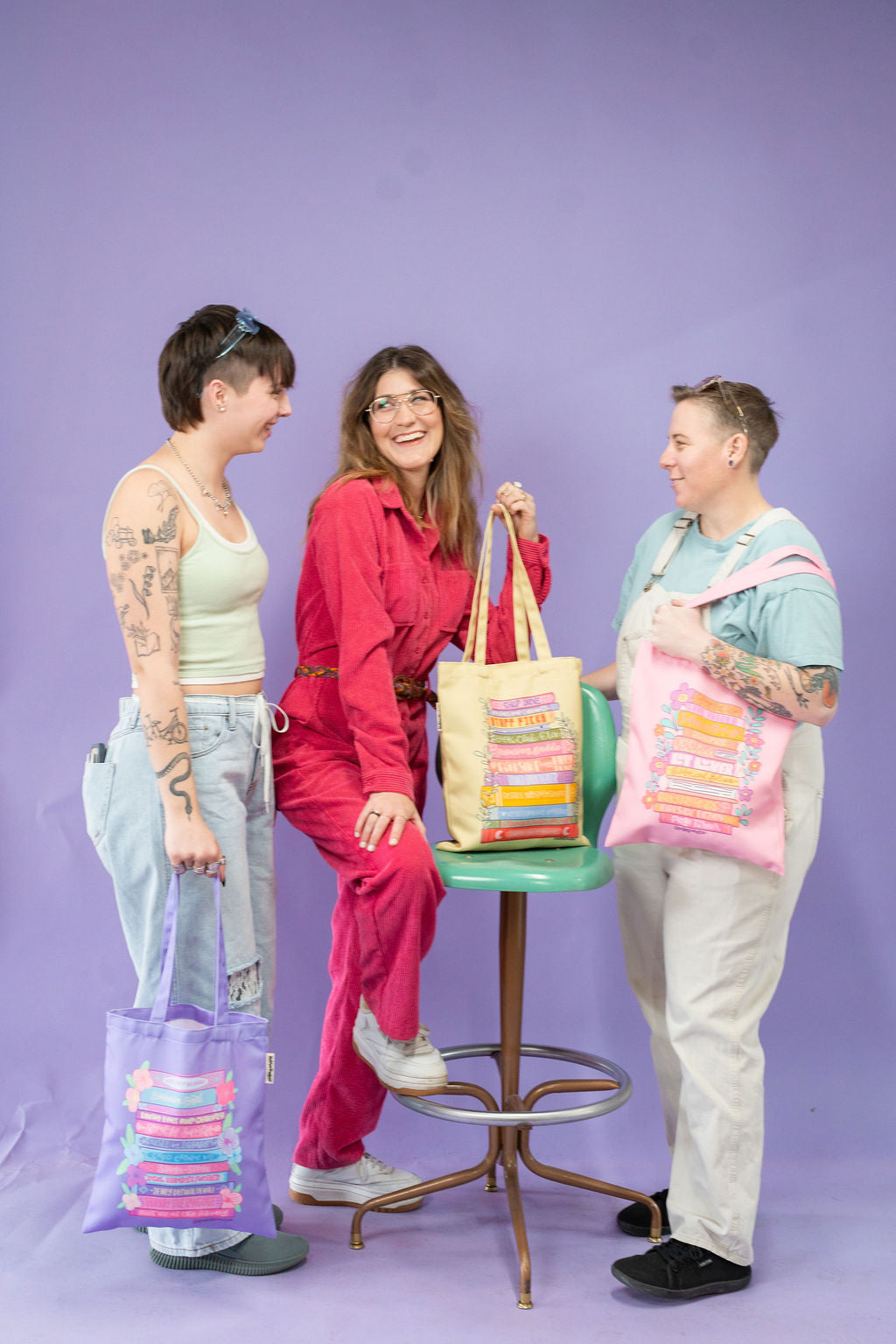 Three people holding colorful tote bags against a purple background