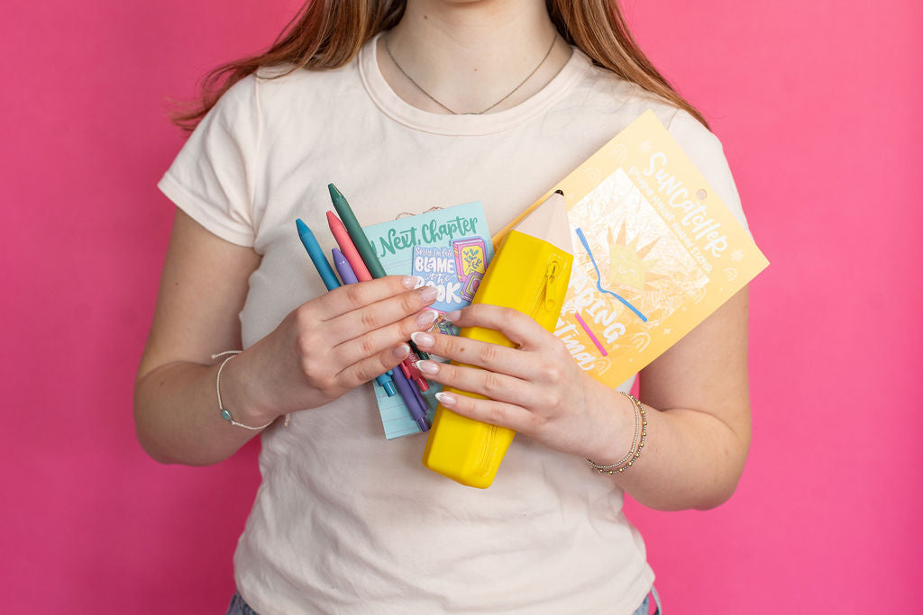 Person holding colorful stationery items against a pink background