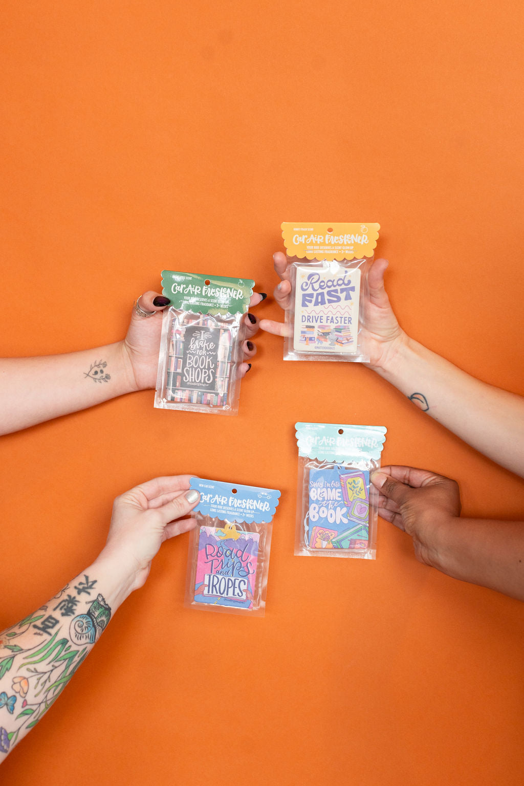 Four hands holding small packages against an orange background