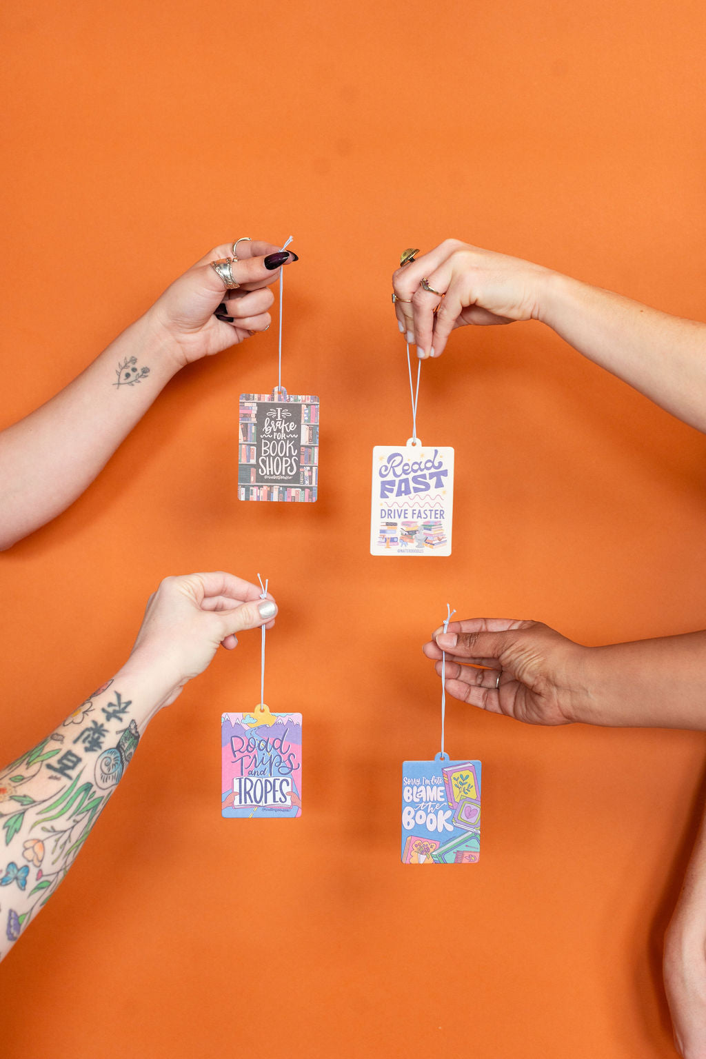 Four hands holding colorful hang tags against an orange background