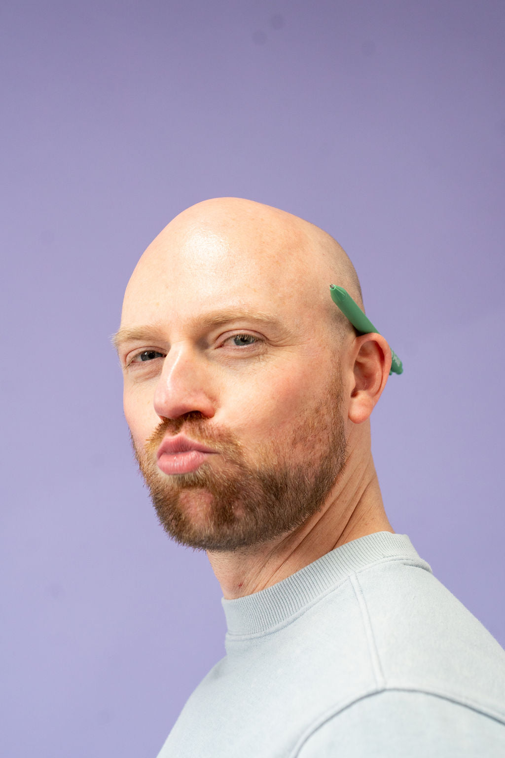 Man with a bald head and beard wearing a green headband against a purple background