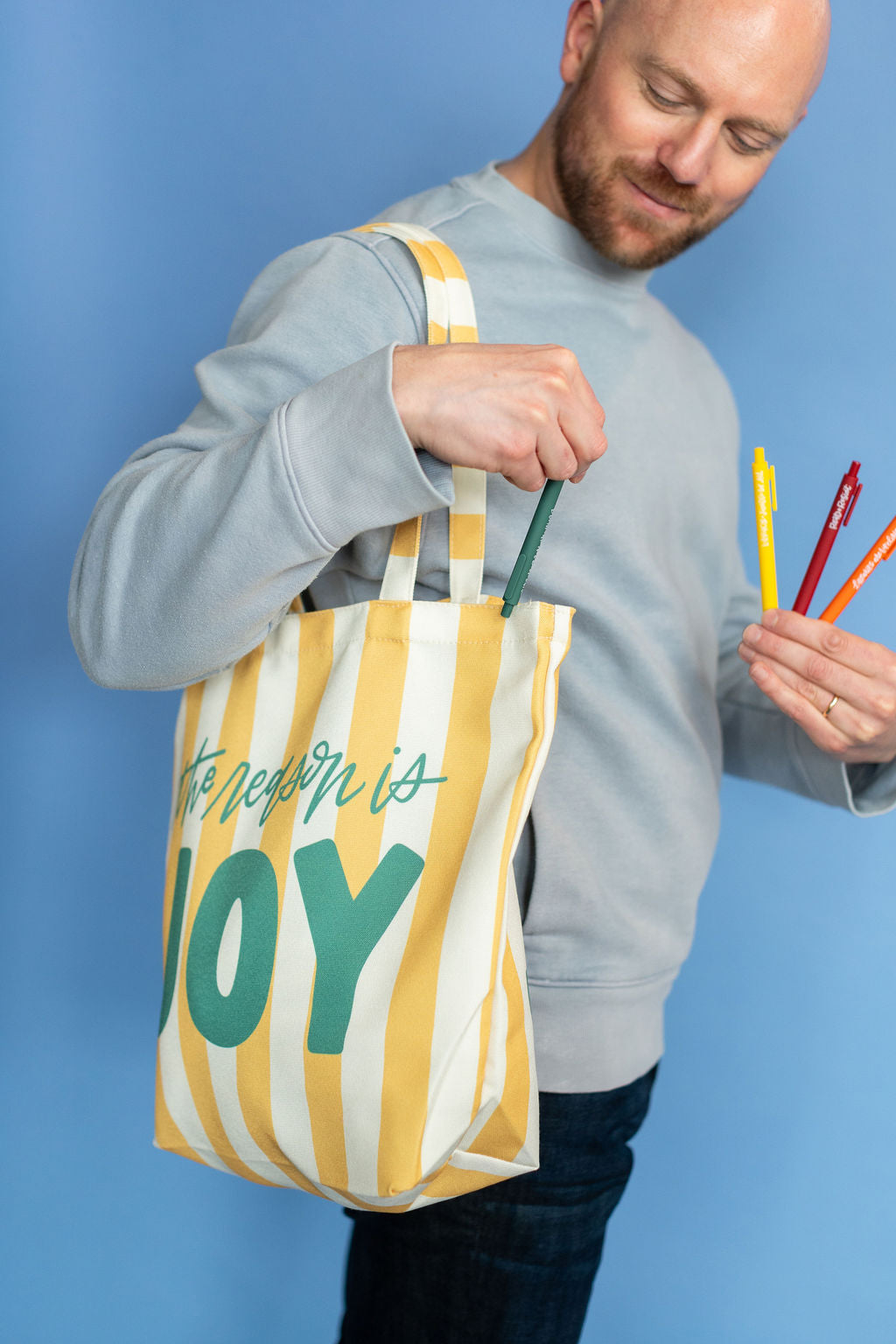 Person holding a tote bag with 'The Answer is Joy' text against a blue background