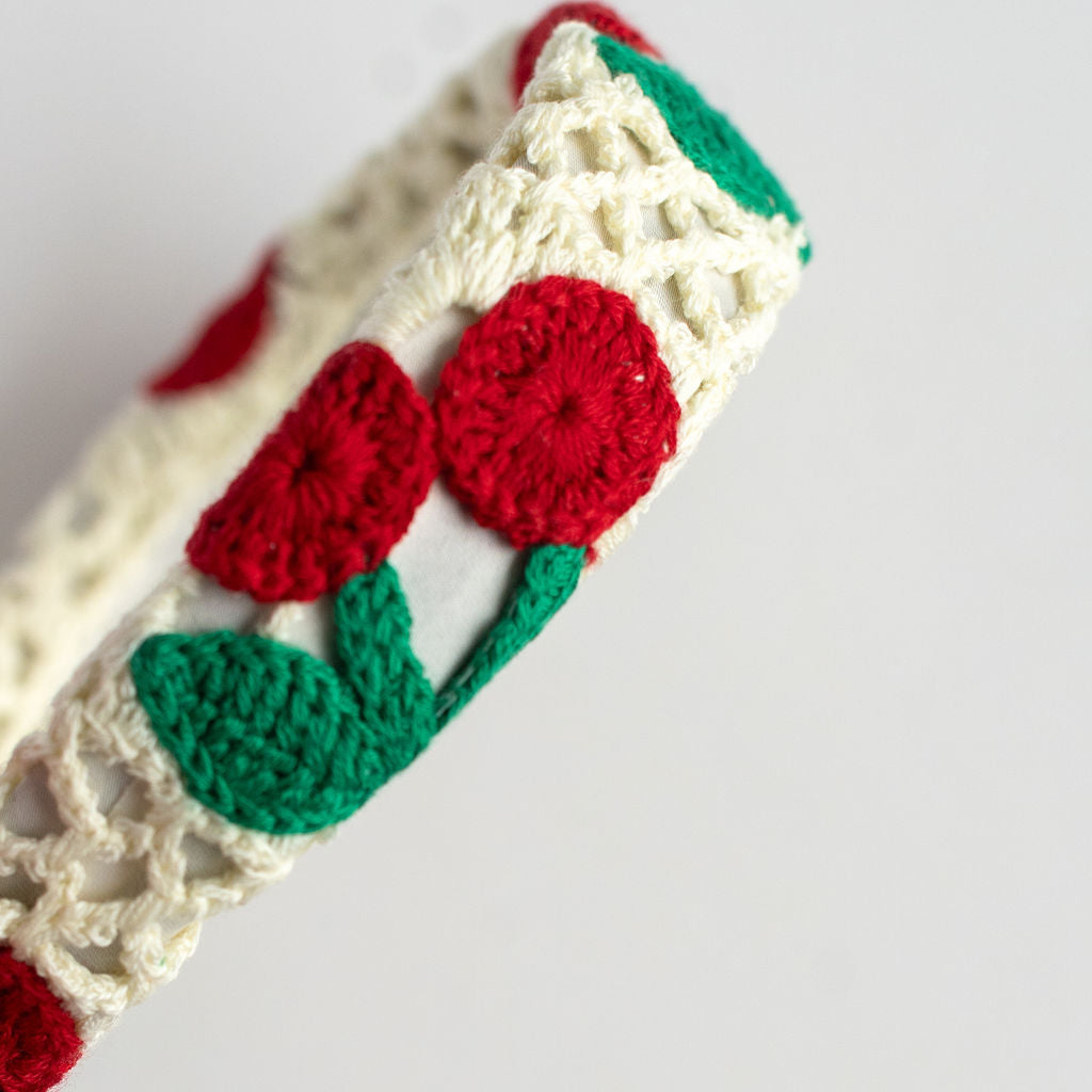 Crocheted headband with red cherries and green leaves on a white background