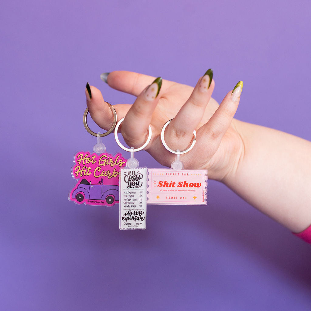 Hand holding keychains with humorous text against a purple background