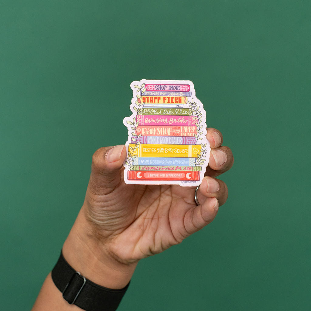 Hand holding a colorful book stack sticker against a green background