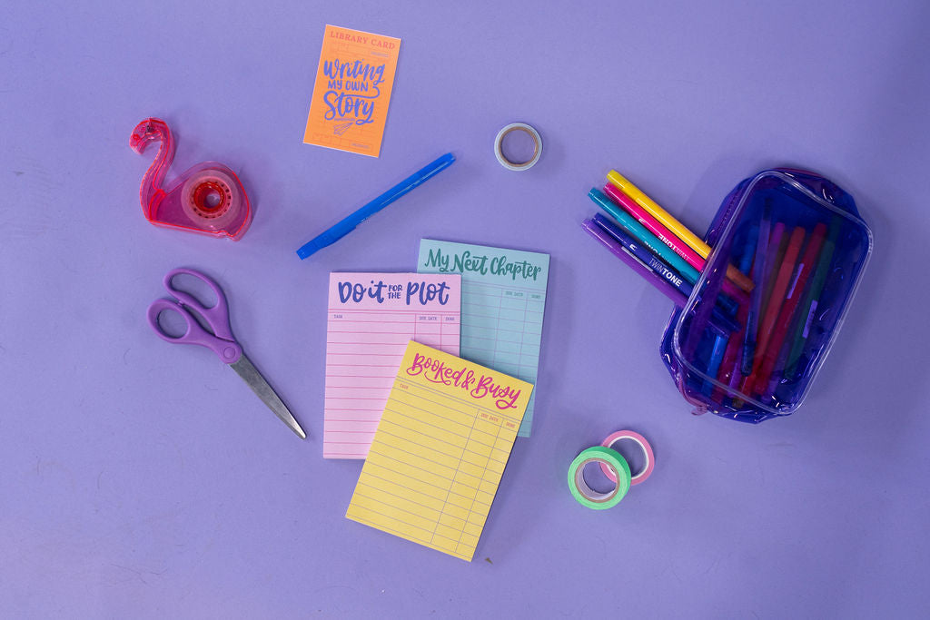 Assorted stationery items including scissors, pens, and sticky notes on a purple background