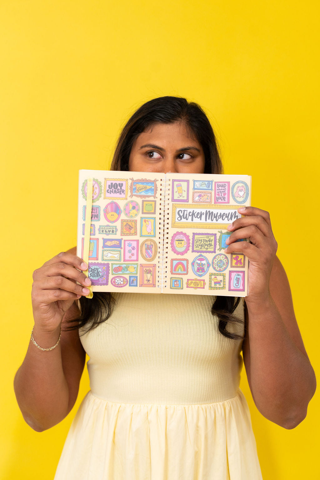 Woman holding a colorful planner with stickers against a yellow background