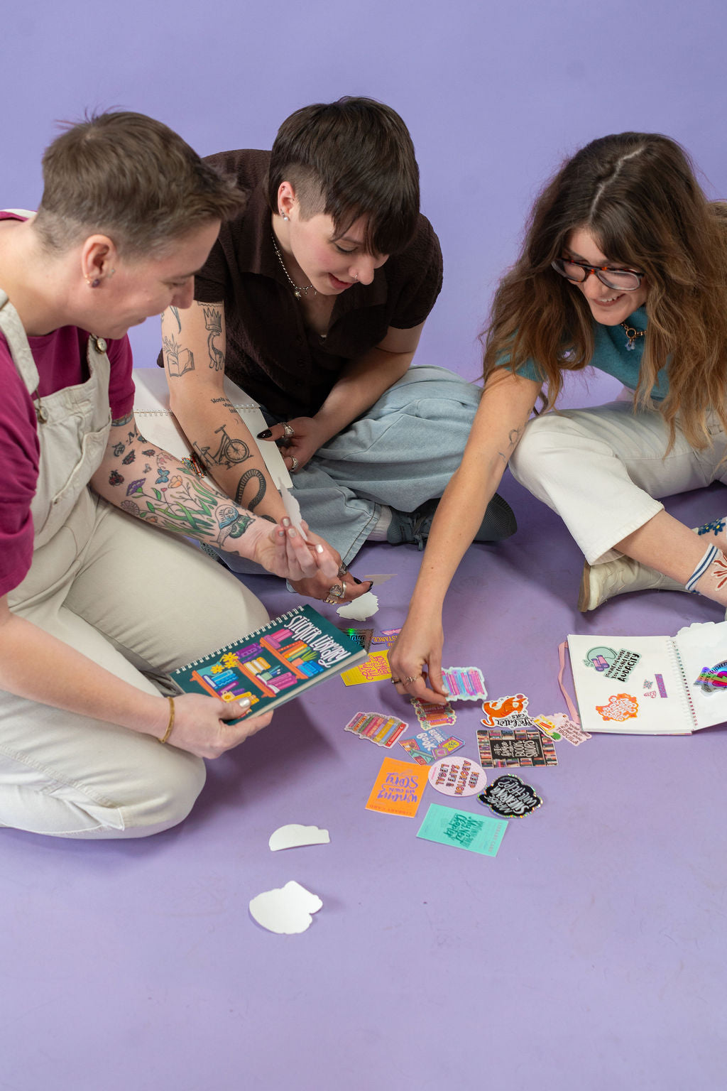 Three people sitting on a purple floor trading stickers