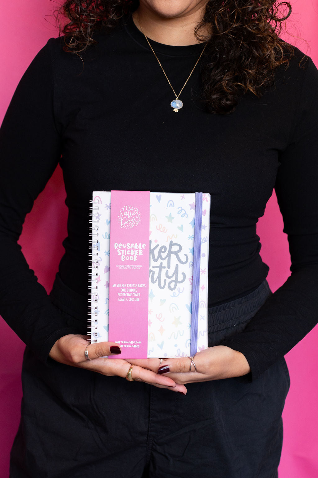 Person holding a colorful notebook against a pink background