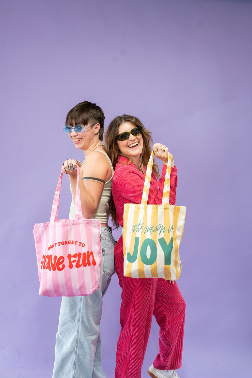 Two people holding colorful tote bags with text against a purple background
