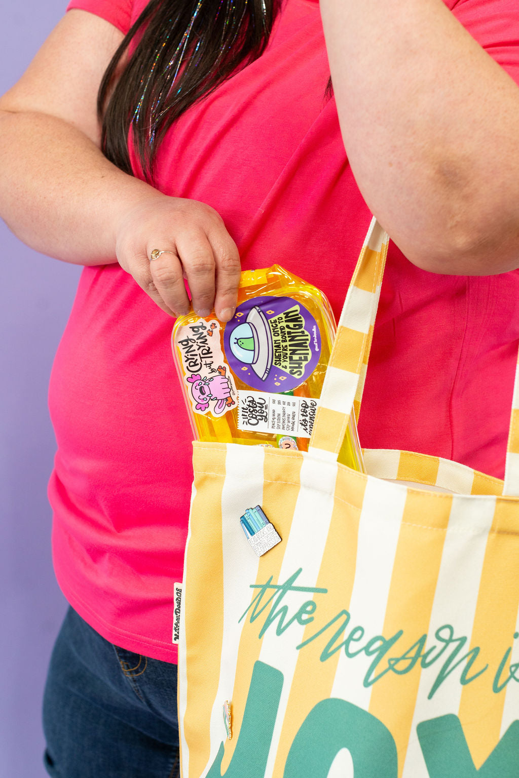 Person holding a yellow and white striped bag with text, wearing a red shirt.